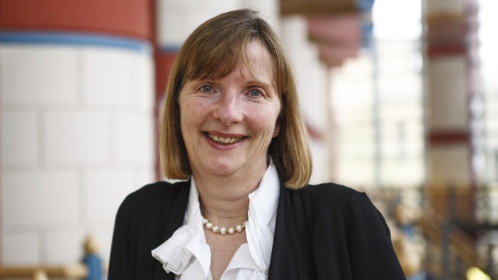 Headshot of Dr. Helen Haugh, smiling in a professional setting with a soft-focus background.