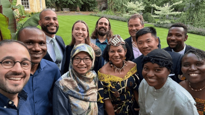 Group photo featuring diverse individuals smiling at an outdoor event with greenery in the background.